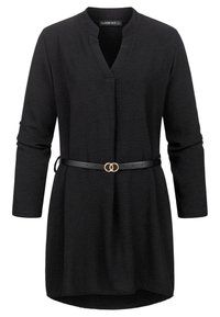 Tunique noire à manches longues avec un décolleté en V et une fine ceinture noire ornée de deux anneaux dorés entrelacés à la taille.