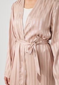 Lichtroze satijnen huisjas met verticale strepen, voorzien van een strikgordel en wijde mouwen. Gladde textuur met een licht reflecterende afwerking.