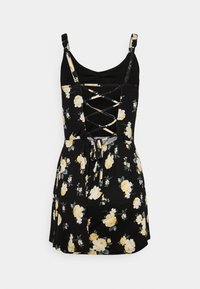 Robe noire sans manches avec imprimé floral jaune, dos à lacets et taille cintrée avec un nœud à l'arrière.