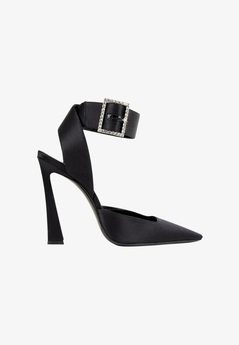 Chaussure à talon haut noire avec bout pointu, bride épaisse à la cheville ornée d'une grande boucle décorée de strass sur fond blanc.