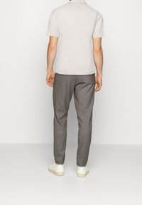 Chemise à manches courtes gris clair, coupe décontractée, associée à un pantalon gris foncé ajusté et des baskets blanches sur un fond neutre.