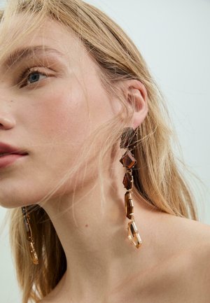 Orecchini pendenti lunghi e geometrici realizzati in resina marrone e metallo dorato, con forme a diamante e ovale per un effetto a strati.