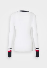 Pull blanc à manches longues côtelé avec poignets rayés noir, blanc et rouge et un bord noir le long de l'encolure, vu de dos.