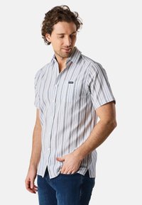 Camicia a maniche corte con bottoni di colore bianco, con righe verticali blu e grigie. Presenta una tasca sul petto e un'etichetta con logo sul lato sinistro.