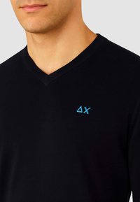 Maglione nero a collo a V con un piccolo logo ricamato blu. La texture è liscia, mettendo in risalto un design aderente adatto per il layering.