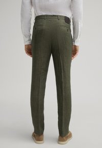 Groene linnen broek met een gestructureerde afwerking, met twee achterzakken en een leren label aan de tailleband, gecombineerd met bruine schoenen.