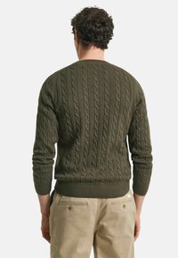 Maglione verde oliva lavorato a maglia con bordo e polsini a costine, caratterizzato da un motivo testurizzato. Indossato al contrario, che mette in evidenza una vestibilità ampia.