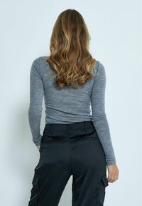 Graues Langarmoberteil aus einem weichen, strukturierten Stoff, kombiniert mit schwarzen Cargo-Hosen, die über Taschen und eine glatte Oberfläche verfügen.