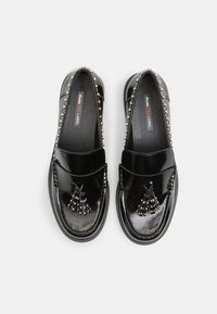 Mocasini negri din piele lăcuită, cu ciucuri decorative, cu nituri argintii pe lateral, și un finisaj neted. Vârf rotund și stil slip-on.