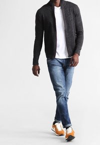 Dark gray zip-up cardigan, white t-shirt, blue jeans, and orange/white sneakers. Simple design with ribbed cuffs and a textured weave.