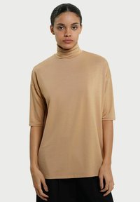Beige turtleneck top lavet af letvægtsstof, med korte ærmer og en afslappet pasform. Materialet har en glat, blød tekstur.