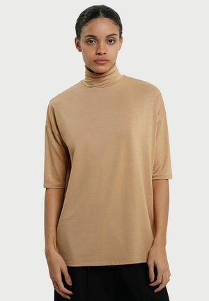 Beige turtleneck top lavet af letvægtsstof, med korte ærmer og en afslappet pasform. Materialet har en glat, blød tekstur.