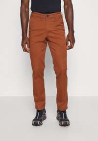 Bruna bomullschinos med rak passform, med knappstängning och fickor. Matcher med svarta träningsskor med orangea detaljer.