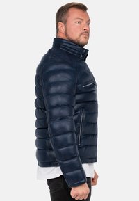 Giubbotto imbottito navy in pelle con colletto alto, tasche con zip e texture trapuntata, caratterizzato da una silhouette aderente e polsini a coste.