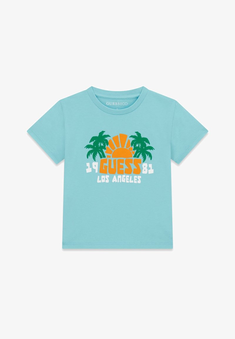 Chemise bleu clair à manches courtes avec un soleil orange, des palmiers verts et le texte « 1981 GUESS LOS ANGELES » sur le devant.