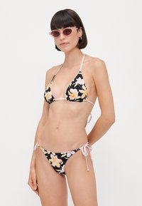 Črni cvetlični bikini z rožnatimi poudarki. Trikotni zgornji del in nastavljivi stranski deli. Tkanina se zdi gladka z živahnim cvetličnim vzorcem.