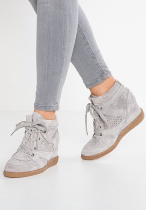 Jasnoszare sneakersy na koturnie zamszowe z perforowanymi detalami i gumowymi podeszwami, noszone z jasnoszarymi wąskimi jeansami.