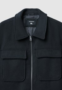 Giacca in pile nera con chiusura a zip, due tasche a toppa davanti e colletto a punta. Etichetta con la scritta "TERRANOVA XL." Texture morbida.