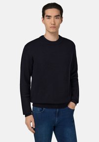 Navy blauwe gebreide trui met een ronde halslijn en ribbelmanchetten, gecombineerd met blauwe jeans. Eenvoudig ontwerp met een relaxte pasvorm.