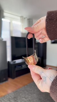 Metalen zilverkleurige beker met een zwart stoffen handvat. Gladde oppervlakte, gebogen vorm, met een glanzende afwerking zonder patronen of accenten.