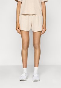 Top en tricot beige à côtes et short assorti, avec une coupe décontractée. Le modèle porte des baskets blanches et des chaussettes blanches à longueur de cheville.