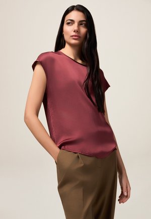 Burgundy silk blouse with short sleeves, straight hem, and a soft sheen, paired with light brown tailored trousers.