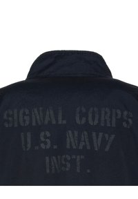 Granatowa kurtka z tkaniny z kołnierzem oraz nadrukowanym tekstem na plecach brzmiącym "SIGNAL CORPS U.S. NAVY INST." w wyraźnej, wyblakłej czcionce.