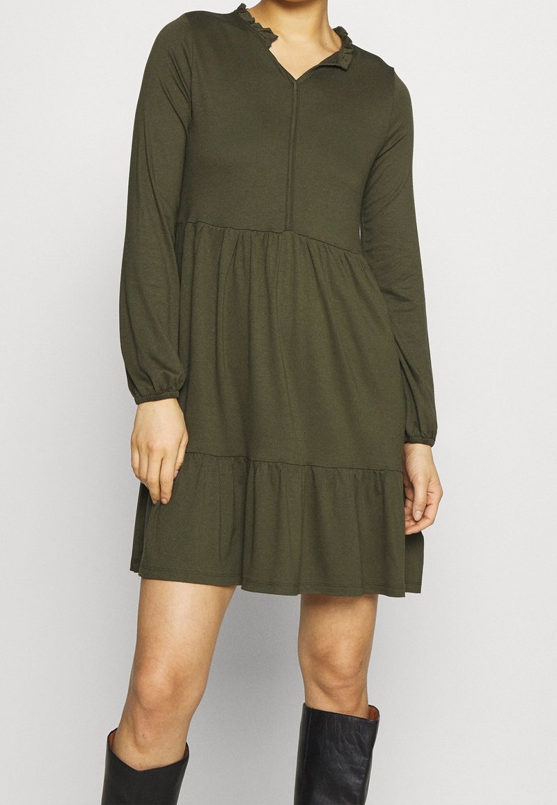 Robe à manches longues, couleur vert olive, avec un col froncé, un décolleté en V et une jupe à volants, fabriquée en tissu doux.