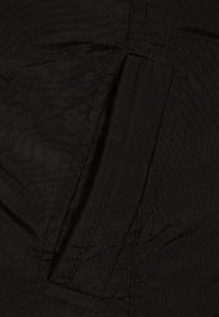 Czarna tkanina o gładkiej strukturze z ukrytą kieszenią na zamek błyskawiczny, wzmocnionymi szwami i lekko pomarszczonym wyglądem.