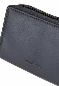 Black textured leather wallet with a zip closure, featuring embossed "MAÎTRE" logo. Compact design with neat stitching detail.