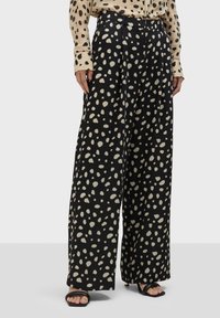 Čierne široké nohavice s béžovým nepravidelným bodkovaným vzorom, s vysokým pásom a mäkkým materiálom. Minimalistické čierne sandále dopĺňajú vzhľad.