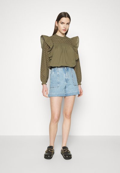 Blouse vert olive avec épaules volantées et détails en dentelle, assortie à un short en denim bleu clair taille haute et des sabots noirs.