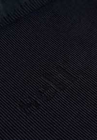 Tessuto blu scuro a costine con superficie testurizzata. Presenta un logo o motivo in rilievo sottile. Il materiale sembra morbido e durevole.