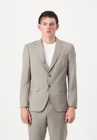 Fato cinza claro com um casaco ajustado, lapelas em bico e dois botões. Combinado com uma t-shirt branca, apresentando uma textura suave e um corte moderno.