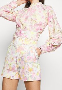 Ensemble blouse et short à motif floral dans des tons pastel de rose, jaune et blanc. Comprend une bordure en dentelle et des manches bouffantes, avec une taille cintrée.