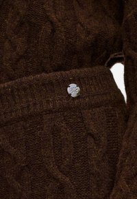 Smeđi džemper od pletenice s detaljima koji prikazuju teksturirani uzorak i dugme u srebrnoj boji na pojasu. Mekana, topla tkanina.