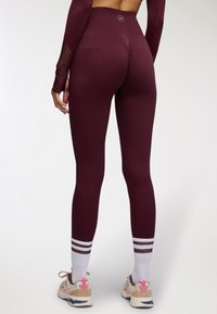 Leggings bordeaux a vita alta con un design senza cuciture, dettagli in mesh testurizzato e strisce bianche alla caviglia.
