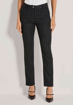 Vrouw in zwarte pinstripe rechte broek met een knoop- en ritssluiting aan de voorkant, gecombineerd met zwarte Mary Jane hakken.