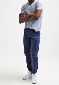 Modrý texturovaný V-krční tričko s krátkými rukávy, spárované s námořnickými joggery s elastickými manžetami a bílými teniskami. Minimalistický design, volný střih.