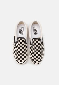 Chaussures à enfiler en toile à damier noir et crème, intérieur blanc, avec détails de couture noirs le long des bords.