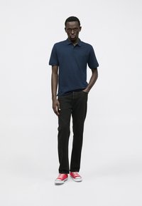 Polo shirt marine à manches courtes, associé à un jean noir et des baskets rouges. Le tissu est lisse, avec un col classique et une coupe ajustée.