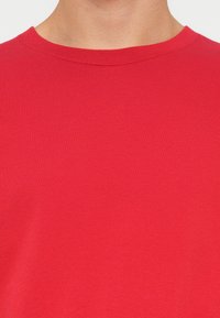 Červené bavlněné tričko s kulatým výstřihem, které má hladkou strukturu a jednoduchý, jednobarevný design, bez vzorů a akcentů.