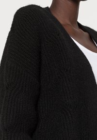 Cardigan nero a maglia con un motivo testurizzato, caratterizzato da scollo a V e apertura frontale, realizzato in un materiale morbido e caldo.