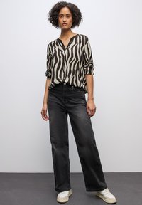 Schwarz-beige gestreifte Bluse mit V-Ausschnitt und aufgerollten Ärmeln, kombiniert mit hoch taillierten schwarzen Jeans und weißen Sneakern.