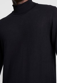 Schwarzer Rollkragenpullover mit einer eng anliegenden Passform, feiner Rippstruktur und langen Ärmeln, ausgestattet mit einem hohen Kragen und glatter Oberfläche.