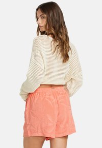 Virkat krämfärgad långärmad topp i kombination med korallfärgade shorts med ett strukturerat palmbladsmönster och elastisk midja.