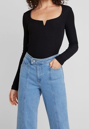 Un haut noir à manches longues avec un décolleté en V et une texture côtelée, associé à un jean en denim bleu clair à jambes larges, taille haute et poches avant.