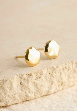 Goldfarbene Ohrstecker mit einer strukturierten, organischen Form und polierter Oberfläche, die auf einer hellbeigen Steinschicht ruhen.