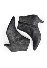 Botas negras hasta el tobillo hechas de material texturizado, con una punta alta y puntiaguda y un cierre de cremallera en un lado. Tacón pequeño y grueso.