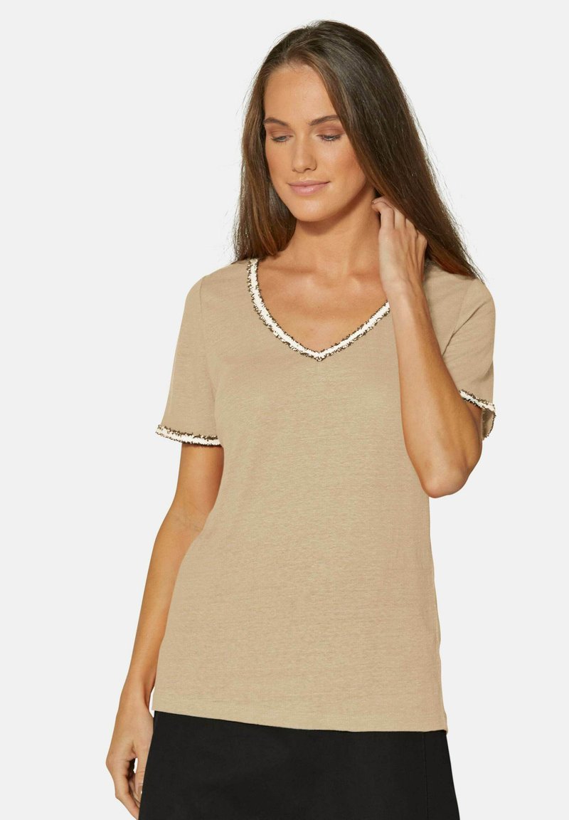 Beige T-shirt met korte mouwen en een V-hals, met een contrasterende zwart-wit bies langs de halslijn en mouwen. Zachte textuur.